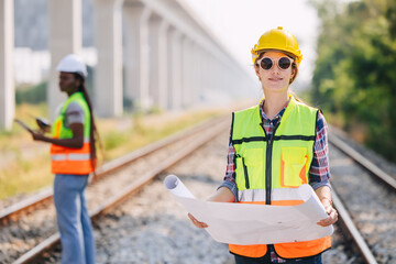 Portrait engineer women on railway tracks construction site with blueprint roll working project...