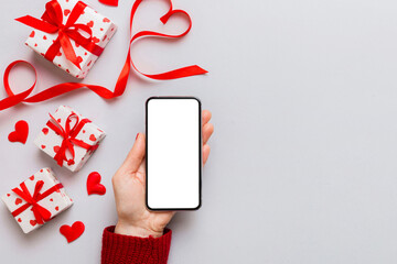 Woman hand holding mobile phone with blank screen on colored background with hearts, valentine day...