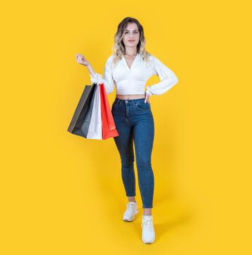 Woman holding shopping bags, full length body size view young attractive woman holding shopping bags. Isolated yellow background. Buy, purchase, consumerism  concept idea image. Copy space.