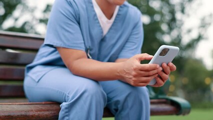 Nurse, typing and cellphone on bench in park, outdoor and internet connection for networking in city. Healthcare employee, hands or mobile phone for message, email or digital app in nature in town - Powered by Adobe