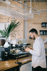 A barista near an espresso machine prepares delicious coffee. A young man prepares coffee in a cafe.