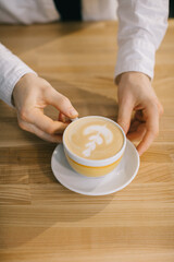 The hands of the barista are holding a delicious cappuccino. Close up, top view.