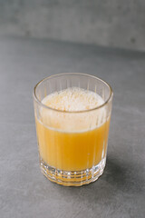 Close up of a glass of orange juice on a gray stone background.