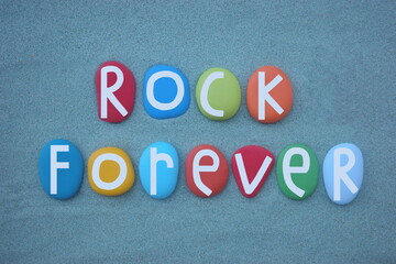 Rock forever, creative slogan composed with hand painted multi colored stone letters over green sand
