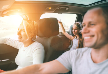 Happy young couple with daughter inside the modern car with panoramic roof during auto trop. They are smiling, laughing during road trip. Family values, traveling concepts.. - Powered by Adobe