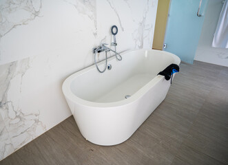 White bathtub in the bathroom. White walls with a pattern. Brown floor.