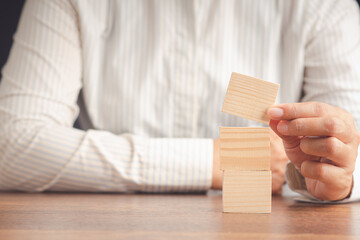 Close-up of a businesswoman's hand holding blank wooden cubes stacked on a wooden table.
