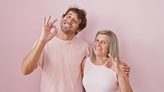 Smiling mother and son, standing together, gesturing an excellent 'ok' sign with fingers over an isolated pink background. full of joy, they're the symbol of a happy, confident, successful family