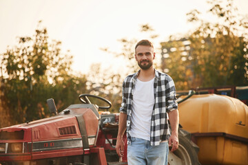 Farmer is casual clothes is standing near little tractor outdoors