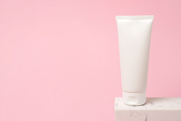 White cosmetic tube staying on the stone podium, pink background with copy space