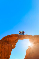 Group of young hikers looking at the landscape from the top of an arch shape in the rock - People trekking in an arid landscape