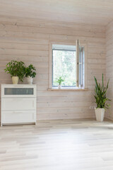 Open window in a room with indoor plants and a chest of drawers in a wooden house