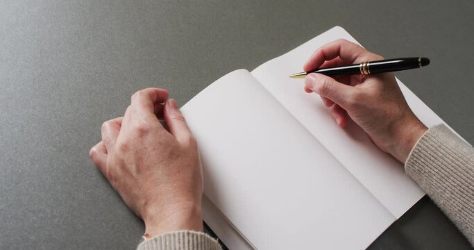 Close up of hands writing with pen on book with copy space on gray background in slow motion