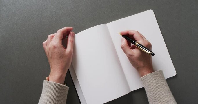 Close up of hands writing with pen on book with copy space on gray background in slow motion