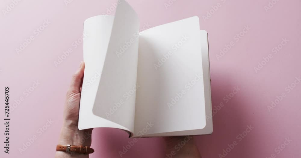 Poster close up of hand leafing through book with copy space on pink background in slow motion