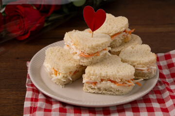 Heart shaped sandwiches made of salad sitting on a white dish on a red and white checkered cloth. There is a roses bouquet on the background. saint Valentines' food. Horizontal image