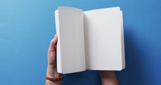 Close up of hand leafing through book with copy space on blue background in slow motion