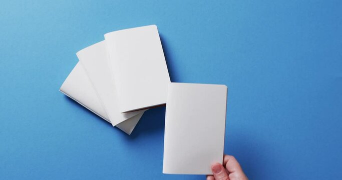 Hand holding piece of paper over pieces of paper with copy space on blue background in slow motion