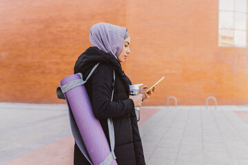 Arab woman looking at her cell phone while walking on the way to her yoga class carrying her mat