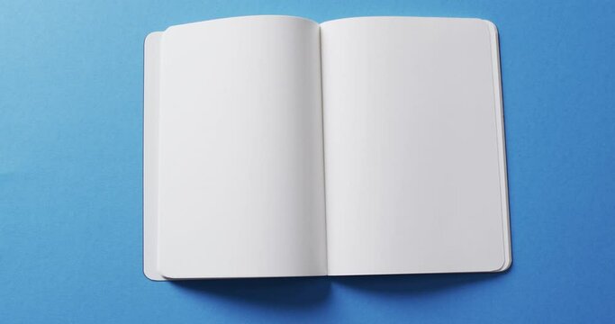 Close up of open blank book with copy space on blue background in slow motion