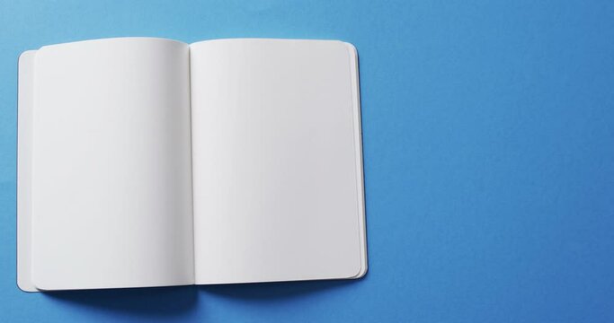 Close up of open blank book with copy space on blue background in slow motion