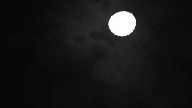 Moon in the sky with clouds at night. The moon hangs motionless while black clouds fly past it. 
