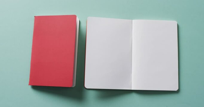 Close up of open blank book and closed red book with copy space on green background in slow motion