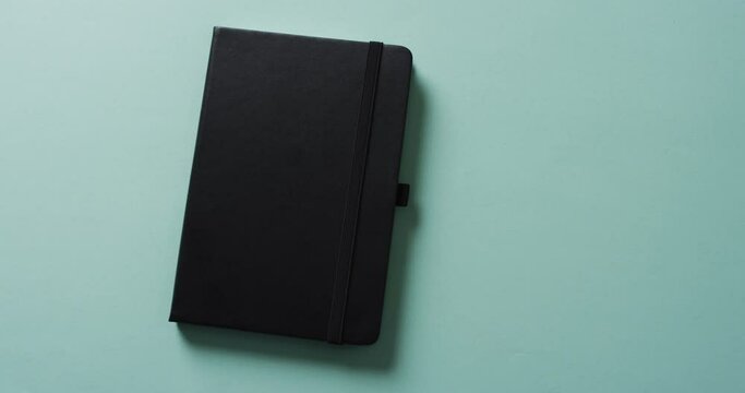Close up of closed black notebook with copy space on green background in slow motion