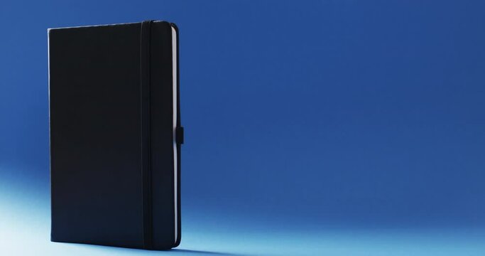 Closed black notebook standing vertical with copy space on blue background in slow motion