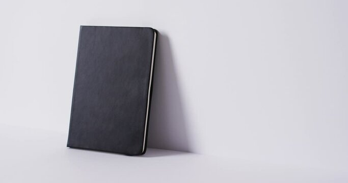 Close up of closed black book leaning on wall with copy space on white background in slow motion