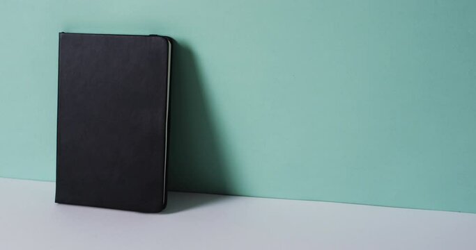 Close up of closed black book leaning on wall with copy space on green background in slow motion