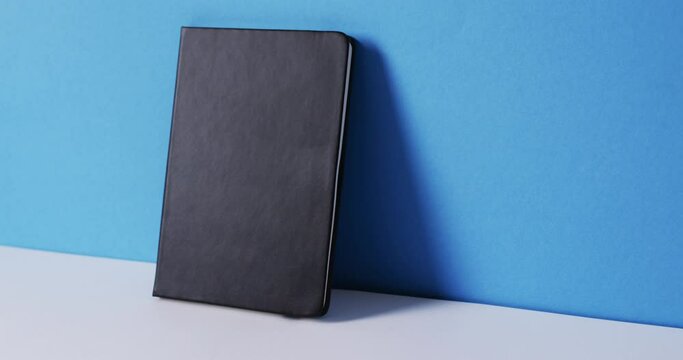Close up of closed black book leaning on wall with copy space on blue background in slow motion