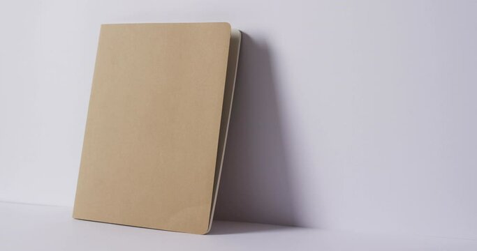 Close up of closed beige book leaning on wall with copy space on white background in slow motion