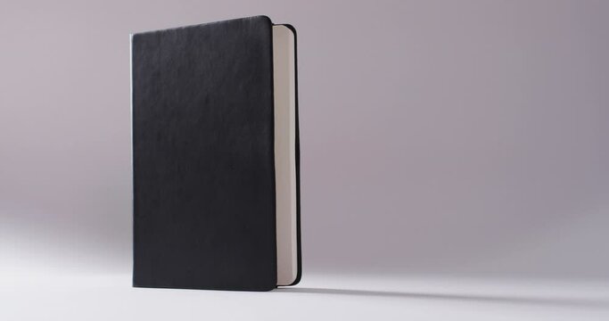Close up of open black book standing vertical with copy space on white background in slow motion