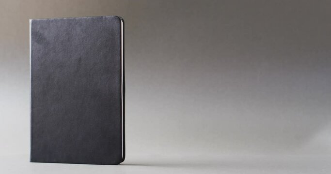 Close up of closed black book standing vertical with copy space on gray background in slow motion