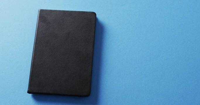 Close up of closed black book with copy space on blue background in slow motion