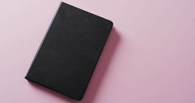 Close up of closed black book with copy space on pink background in slow motion