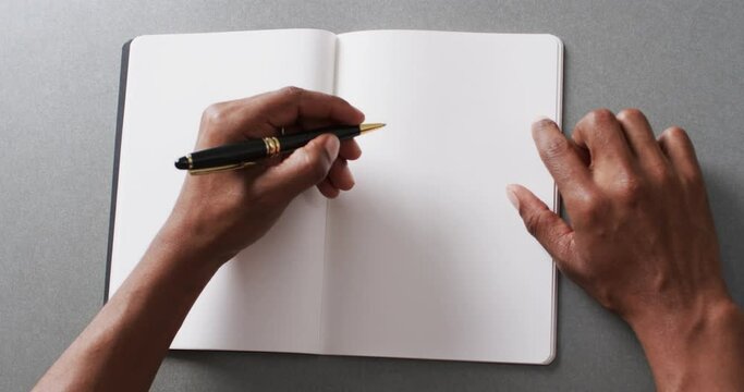 Close up of hand writing with pen on book with copy space on gray background in slow motion