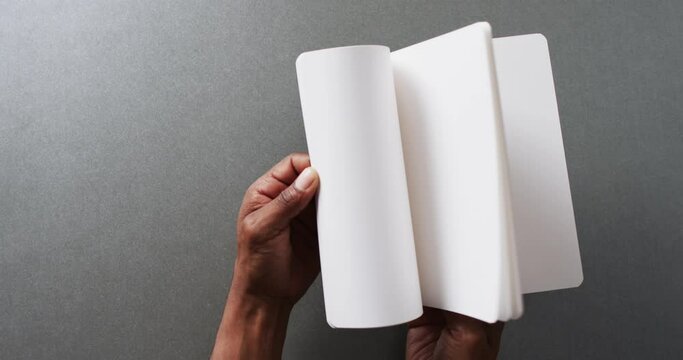 Close up of hand leafing through book with copy space on gray background in slow motion