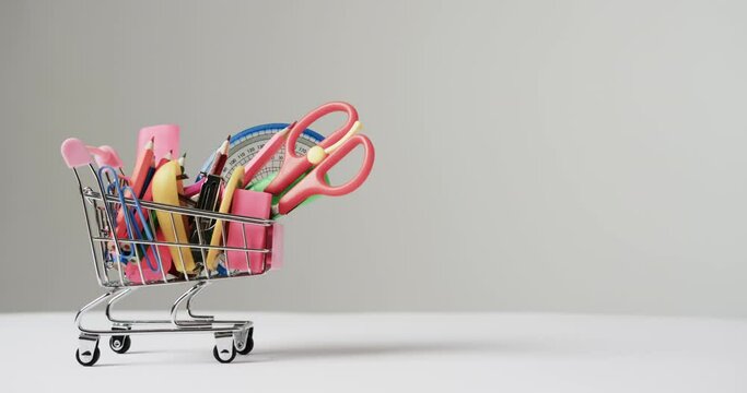Close up of miniature shopping trolley school materials and copy space on grey background
