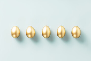 a row of golden eggs on a blue background top view flat lay