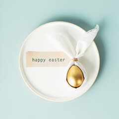 golden egg in easter bunny napkin on white plate over blue background