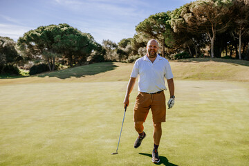 Sotogrante, Spain - January 25, 2024 - A golfer in a white shirt and tan shorts gestures with a putter on the green with trees in the background.