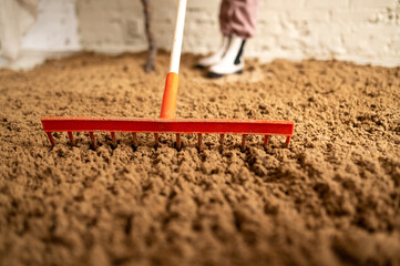 A rake spreading sand on a brick background. Construction or earthworks concept