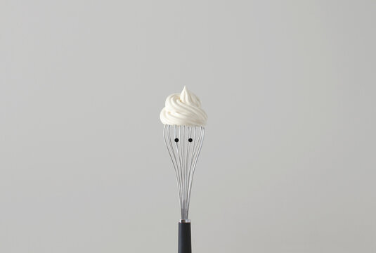 Conceptual portrait of a face with a cool hairstyle made from Whipped Cream On a Whisk With Black Dot Eyes
