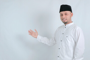 Asian Muslim man smiling to give greeting during Ramadan and Eid Al Fitr celebration over white background.