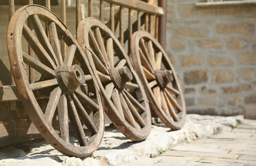 Three old wooden wheels for horse carts leaning against a wooden wall in perspective