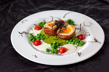 Fried egg Scottish eggs with green peas and sauce on a white plate in a restaurant