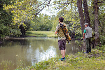 Two fishermen with fishing tackles standing on the beautiful river bank and swinging rods to catch a fish. Sport fishing concept.