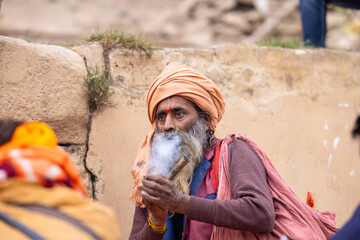 Indian holy old sadhu smoking during the kumbh fair during winter day in traditional dress.	